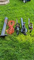 Yardworks leaf blower with detachable nozzle, orange extension cord, Toro edger and Craftsman hedge trimmer laid out on grass