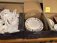 Two boxes containing ceramic plates and teacups wrapped in tissue paper, showing floral pattern on edges of plates.