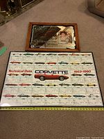 Both framed posters laid on carpet, showing the Coca-Cola and Corvette designs clearly.