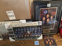 Three framed posters/signs arranged including World Cup 2006 Champions soccer poster, 2011 Hockey Induction Celebration poster with signatures, Lamborghini Murcielago sign partially visible