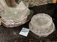 Photo of various stacked glass serving dishes and bowls showing different shapes and textures including scalloped and embossed designs.
