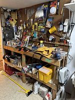 Wide view of wooden workbench with shelving and tools hanging on pegboard above and around it, including clamps, wrenches, and storage bins under the bench.