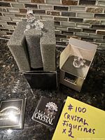 Two crystal clown figurines with original boxes, protective foam, and included booklets on kitchen counter against mosaic tile backsplash.