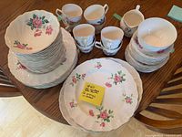 Full view of the assembled 56-piece set including dinner plates, bowls, cups, saucers, and creamer, showing the pink rose floral pattern and white ceramic base.