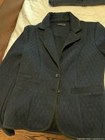 Front view of black quilted blazer with lapel collar and two buttons, laid flat on bed.