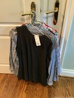 Photo showing 10 ladies tops hung on hangers on a door; includes a black sleeveless top in front.