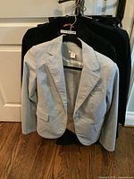Photo of light grey women's blazer hanging on a hanger with two other dark blazers behind.