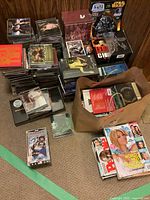 Overview photo showing large stacks and piles of various CDs, DVDs and magazines, along with bags containing more items.