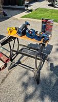 Full view of the power tool set displayed on folding workbench with drills and circular saw.
