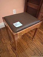 Overall view showing brown leather cushioned top on polished wood frame with tapered legs on hardwood floor