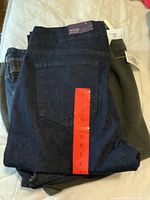 Three folded pants stacked, showing tags and different shades of pants.