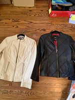Two jackets on hangers laid flat on wooden floor; cream Point Zero jacket on left, black Massimo jacket on right.