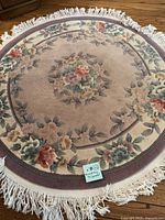 Full image of round wool area rug with floral design and fringe laid on wood floor, showing overall pattern and condition.