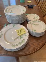 Stack of multiple plates and smaller dishes arranged on a wooden table, showing floral design with scalloped edges.