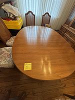 Top view of oval wooden dining table with three chairs visible. Wood has smooth polished finish and slightly visible grain.