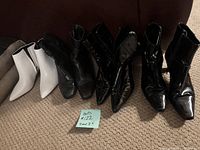 Five pairs of ankle boots including white and black pointed toe styles arranged side by side on carpet.