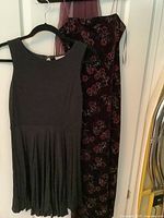 Two evening gowns hanging: black sleeveless Ann Taylor Loft dress and black strapless gown with purple floral pattern from JS Boutique