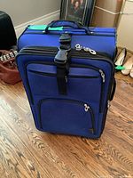 Blue SwissGear softside luggage standing upright on a wood floor with visible front zippered pockets and adjustable strap.