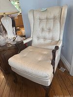 Front angle view showing full chair with its beige upholstery with button tufting and dark wood armrests and legs