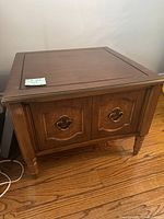 Front view of one brown wooden traditional style side table with panel doors and metal pulls, showing top and front details.