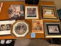 Top-down photo showing seven framed art prints arranged on a wooden table, illustrating variety in size and style of frames and subject matter.