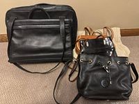 Front angled view of six bags showing mixed styles, sizes and materials primarily black leather with one tan leather backpack and one beige canvas bag.