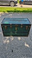 Front view of the vintage green trunk showing metal latch closures and worn green finish with rust on metal parts.