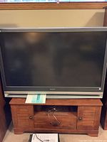 Full view showing the Sony television sitting atop a wooden TV stand with storage compartments.