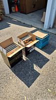 Three boxes of vintage vinyl records placed outside a garage, showing the quantity and packaging type.