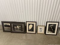 Five framed art pieces arranged on floor showing variety in size, style, and frame type.