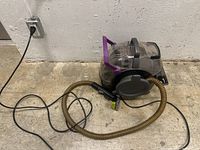 Side view of Bissell portable wet vacuum cleaner with attached hose and cleaning nozzle.