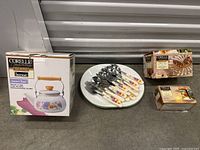 Overview of the lot showing boxed tea kettle, floral flatware set on white plate, and additional boxed items.