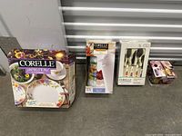 Photo showing all boxed items in lot including Corelle dinnerware set box, thermal server box, flatware set box, and napkin set box.