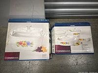 Two original Corning Ware boxes; one showing a square dish, one showing several dishes with floral patterns.