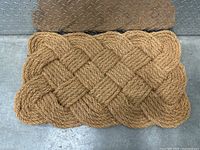 Photo shows a rectangular door mat made of tightly braided natural coir fibers arranged in an overlapping basket weave pattern.