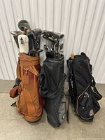 Three golf bags filled with assorted golf clubs standing against wall