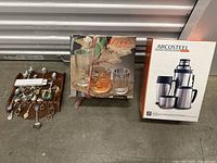 Wooden tray with assorted cutlery spoons, vintage liquor glass set with decanter in decorative box, and boxed Arcosteel Indian beverage set.