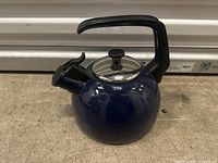 Front view of blue round kettle with handle and lid on concrete surface.