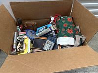 Top view of open cardboard box with all items visible including electronic devices, wallets, game, and holiday textiles.