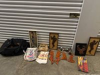 Wide shot of the lot showing framed artwork, metal figurines, cloth and plastic bags, and textile pieces arranged on the floor.