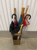 Photo showing seven umbrellas placed inside the wicker umbrella stand against a white industrial wall and floor.