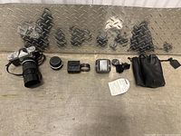 Full overview image showing the Nikkormat camera with telephoto zoom lens, additional lens, leather case, external flash, camera strap, small accessories, and a receipt or paper.