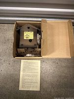 Top view of the vintage wooden cuckoo clock and instruction sheet, showing the clock in a cardboard box with some packing material.
