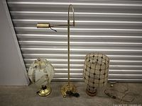 Three vintage lamps placed together showing different styles: brass with glass panel lamp, brass desk lamp, and fabric shade lamp.