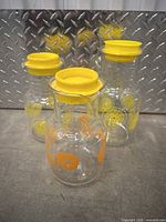 Three vintage Pyrex glass pitchers with yellow rubber lids on concrete floor with metal backdrop