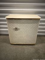 Front view of the vintage white laundry basket showing diamond-patterned exterior, gold trim on top and bottom edges, and star-shaped metal ornament on center front.