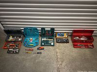 Wide view of the entire tool lot arranged on the floor, showing multiple kits, trays, and toolboxes containing assorted hand tools and hardware.