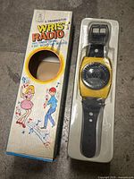 Front view of original box featuring dancing figures and musical notes, with yellow wrist radio visible in window.