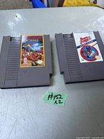 Photo of two vintage Nintendo NES game cartridges on a light-colored surface, showing front labels and cartridge shape.