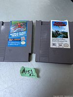 Photo of two vintage gray Nintendo NES cartridges, World Class Track Meet and F-15 Strike Eagle, on a gray surface.